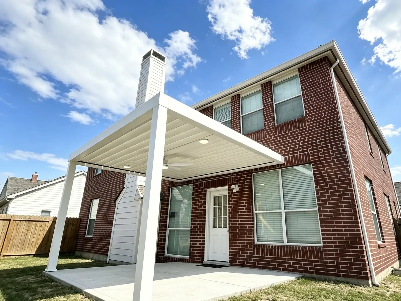 White wall-mounted louvered pergola attached to the side of a brick house